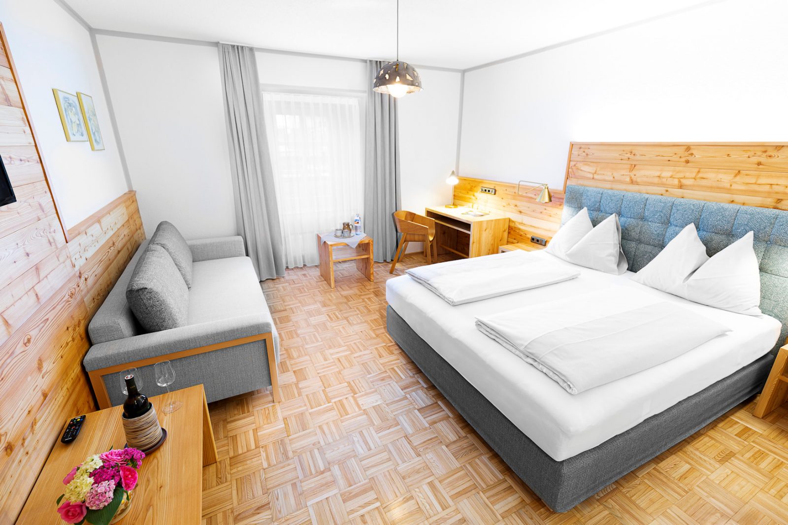 Hotelzimmer mit modernem Boxspringbett, rustikaler Fichtenvertäfelung und Saunakorb. Beläuchtung von Artemide.